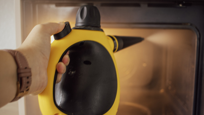 A person using a handheld steamer to clean an oven
