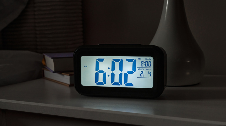 alarm clock on a nightstand with books and a lamp
