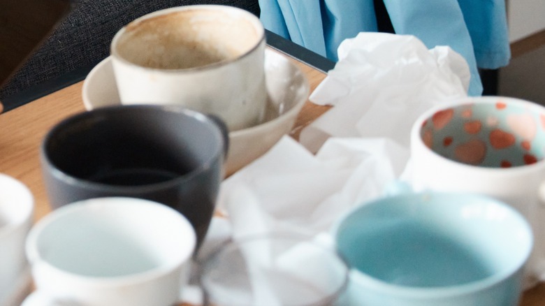 collection of dirty mugs sitting on a nightstand with tissues and napkins