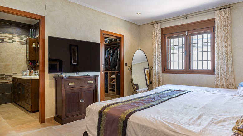 tv on wall of out of style bedroom with neutral colors