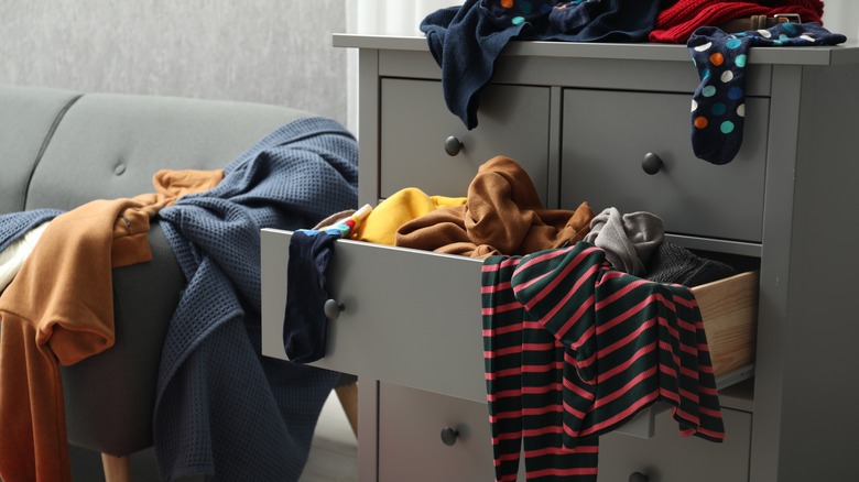 messy grey dresser with clothing falling out of drawers and thrown on top