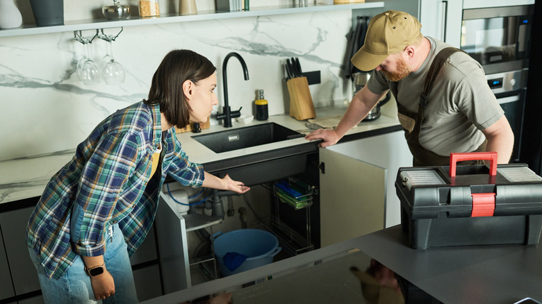 A woman shows a plumber a problem with her kitchen sink