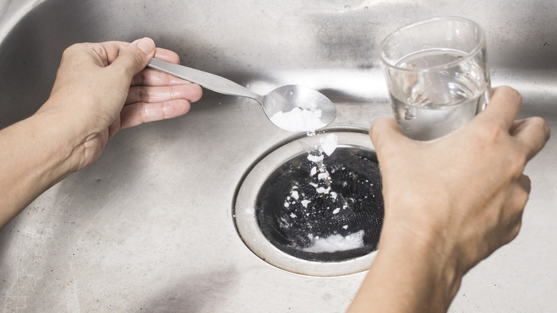A person puts baking soda and vinegar into a clogged stainless steel kitchen sink