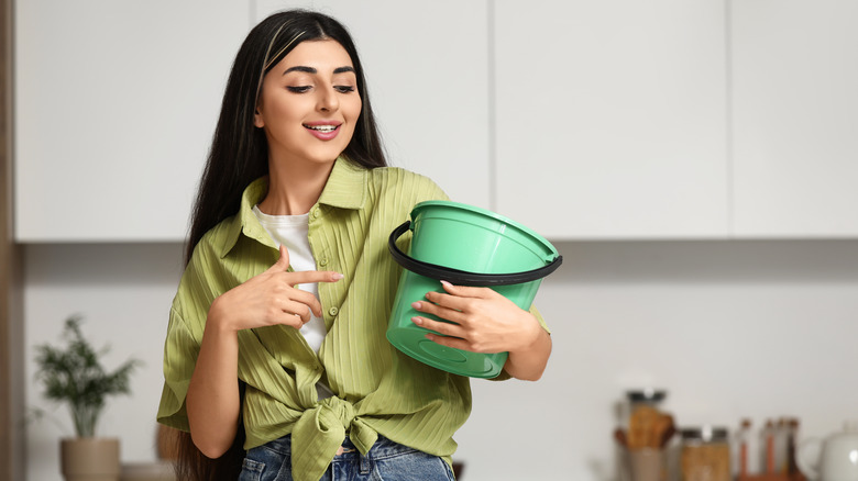 A woman points at a green bucket and smiles