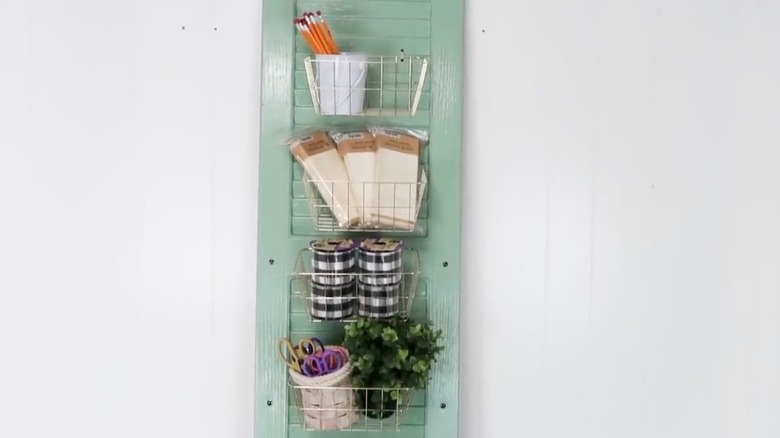 Shutter panel painted green with Dollar Tree baskets attached hanging on a white wall