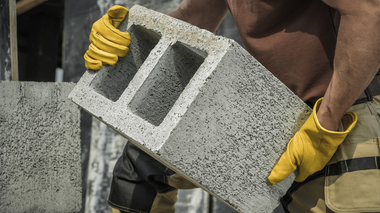 Person holding cinder block with yellow work gloves on.