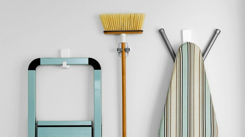 Step ladder, broom, and ironing board hanging from Command hooks on wall