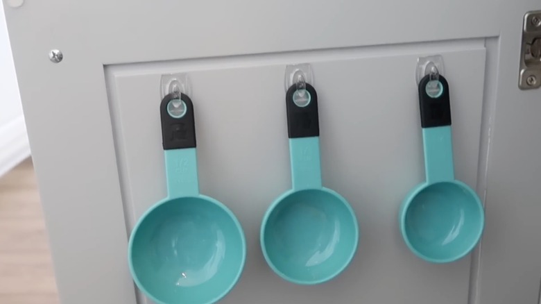 Measuring cups hanging from mini Command hooks in kitchen cabinet