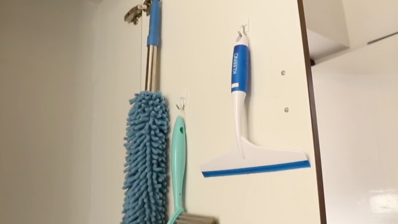 Duster, squeegee, and brush hanging inside cabinet door from Command hooks