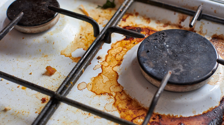 Close-up of two stove burners covered in stains, grease, and debris