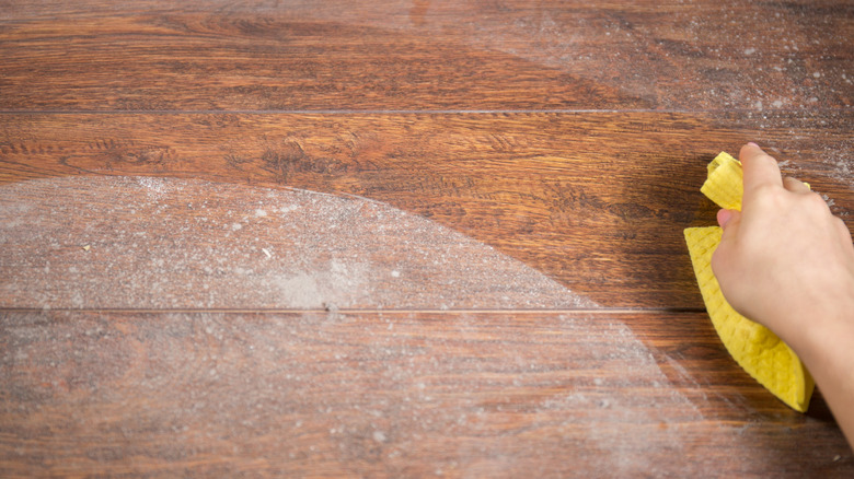 Gloved hand wiping dust off a wood surface with a cloth