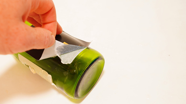 Hand attempts to remove a label from a bottle as it rips