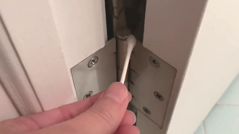 Person applying liquid coconut oil to squeaky door hinge using cotton swab