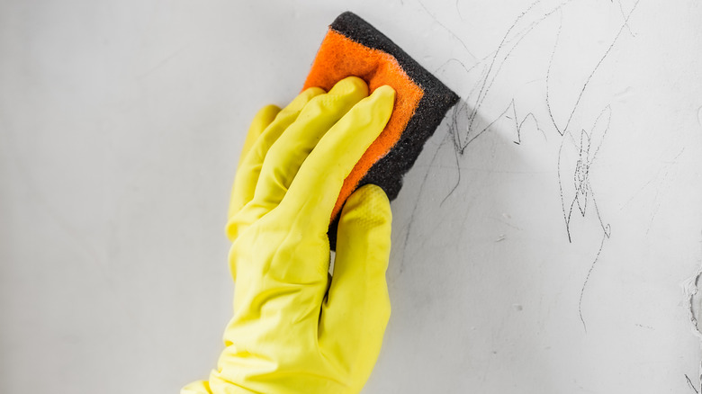 Gloved hand holding a sponge to remove crayon and ink from wall