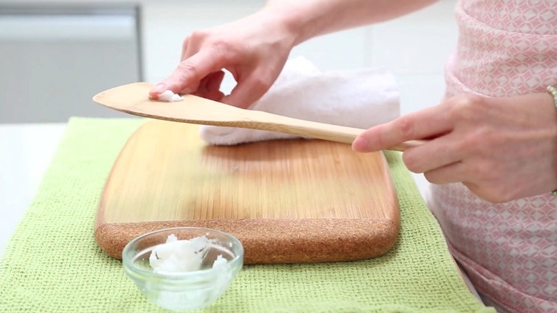 Person conditioning wooden spoon and cutting board with coconut oil
