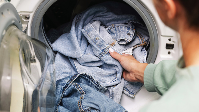 A person adding denim laundry items into a washing machine