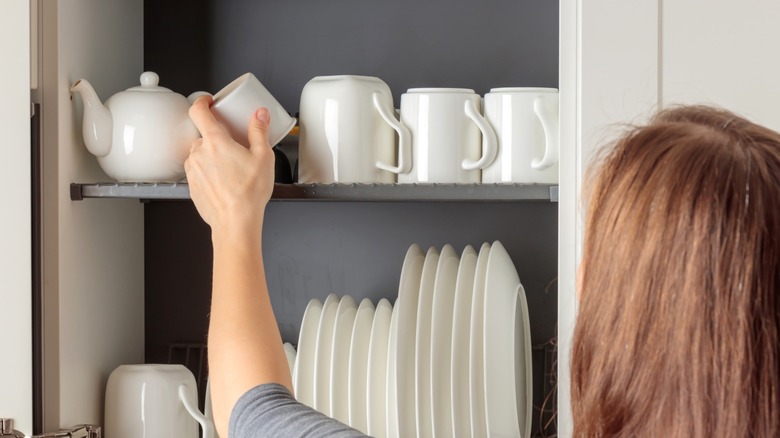 Woman arranging coffee mugs in a kitchen cabinet