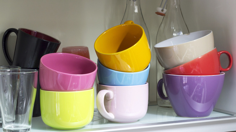 a bunch of stacked colorful coffee mugs in a cabinet