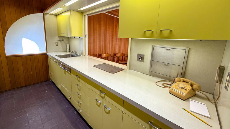 A 1960s kitchen has bright chartreuse cabinets and a rotary phone on the countertop