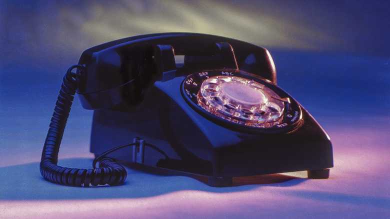 A black rotary phone sits on a surface surrounded by violet light