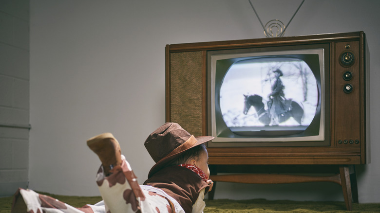 A person wearing a cowboy outfit watches a black and white program on a 1960s television