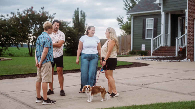 Two couples chatting outside a home on a concrete driveway with patched cracks.