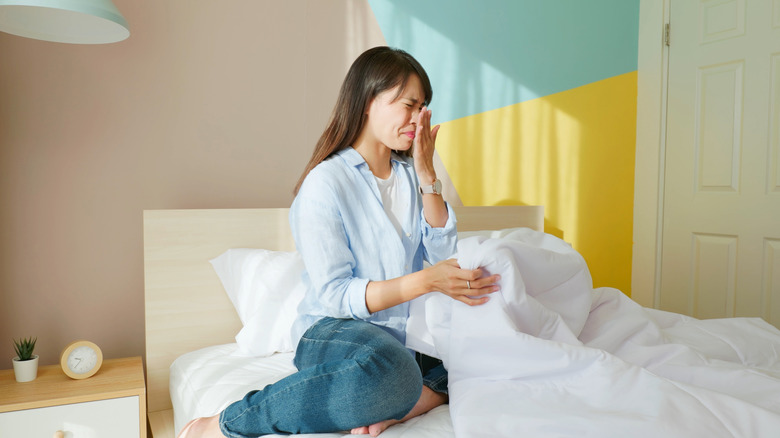 A woman experiencing a bad odor coming from the bed and sheets she's sitting on.