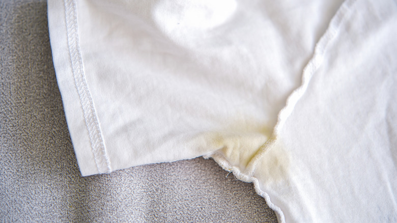 A yellow sweat stain on the underside of a white t-shirt laying on a couch.