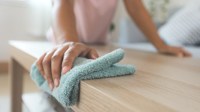 Person wiping down a coffee table with a microfiber cloth
