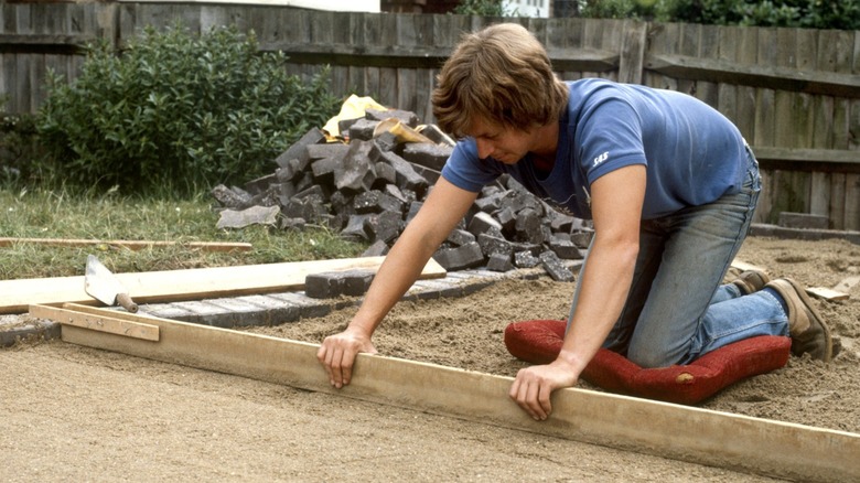 A worker leveling a sand bed for a new patio