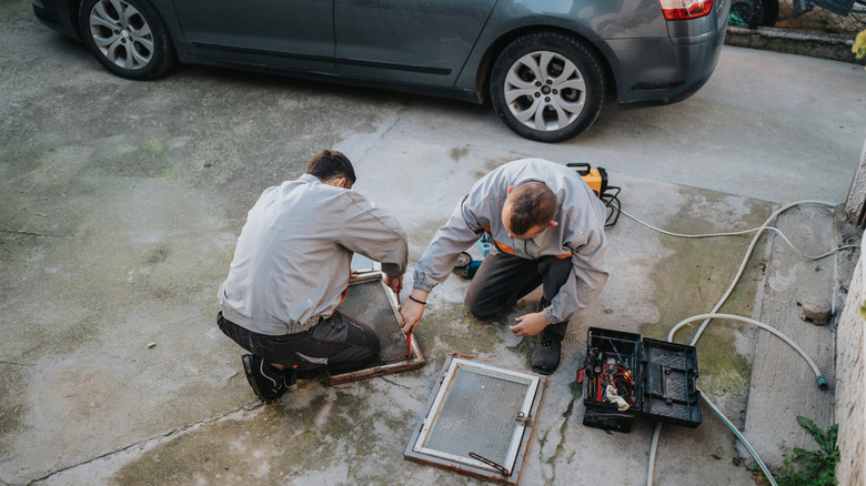 Two technicians work on an outdoor maintenance task on a concrete driveway