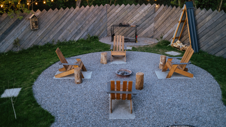 a Gravel patio with rustic seating and central fire pit in fenced garden