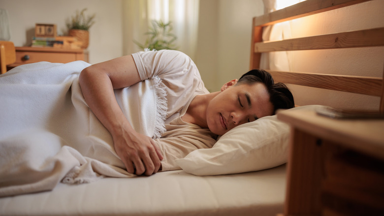 A person sleeping on their side in a bed with white sheets.
