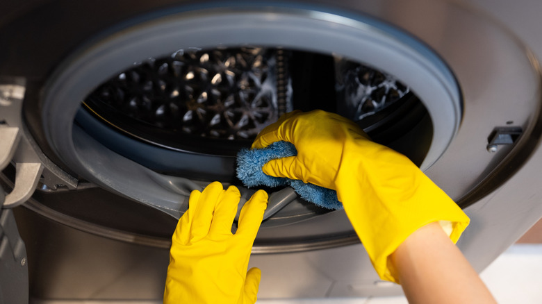 a person in gloves scrubbing washing machine drum