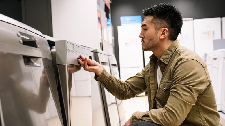 A man examining dishwashers in the appliance section of a home goods store.