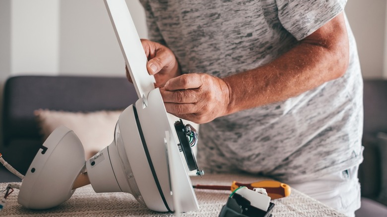 Man assembling a new white ceiling fan in his living room