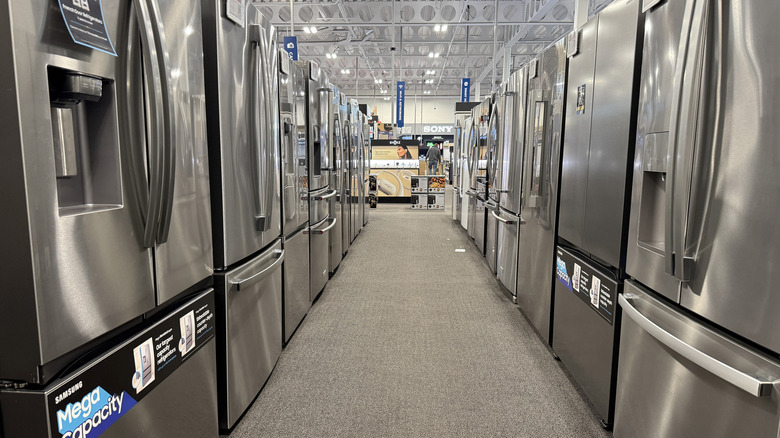 An appliance store aisle full of new stainless steel refrigerators for sale.