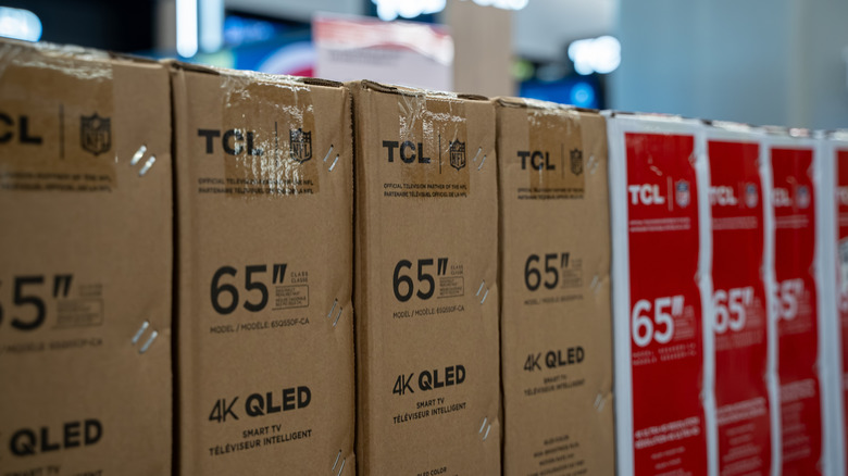 A row of TCL TVs in brown, red, and white boxes inside a store