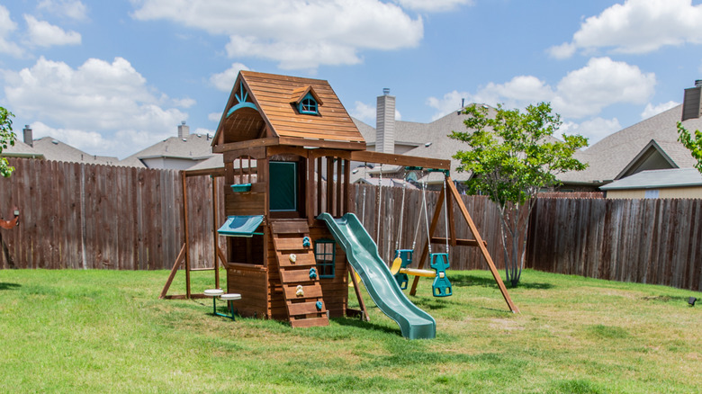 A brown wood backyard playset with swings and slide
