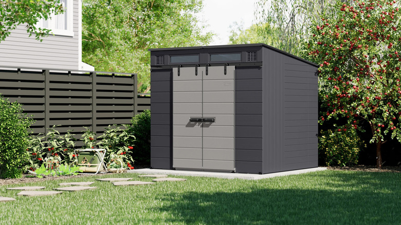 A modern dark gray Suncast shed from Costco sits in a sunny backyard