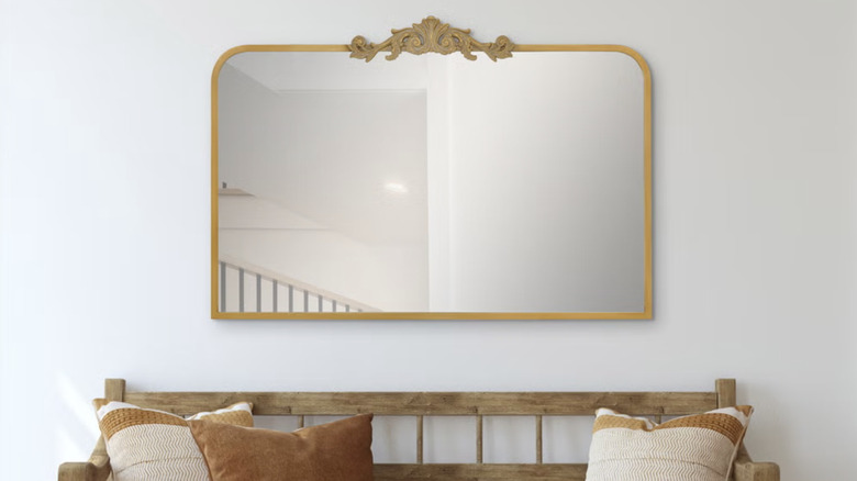 Vintage-style gold mirror in front of a wooden bench with brown and off-white colored pillows.