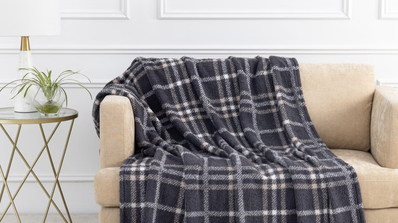 A gray plaid throw blanket draped on a tan couch next to a gold and glass side table.