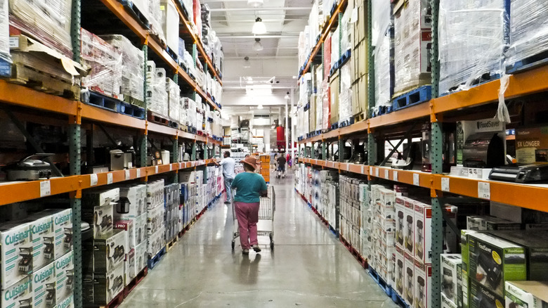 A woman walking with a shopping cart down an aisle in Costco.