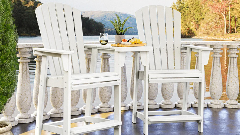 Two white wooden patio chairs flank a tall table in front of a mountain range in the distance