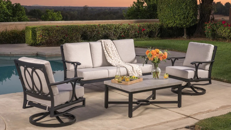 A set of patio furniture sits in front of a backyard pool at dusk