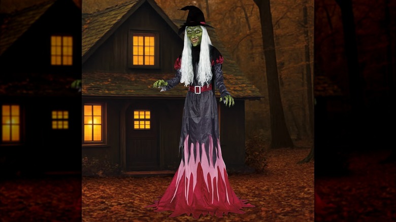 An extremely tall witch with a pointy hat standing in front of a hut