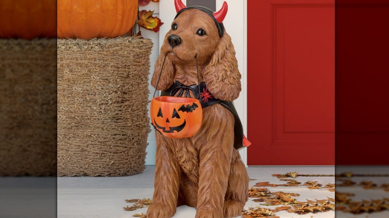 A cute cocker spaniel with a Halloween candy bucket hanging from its mouth