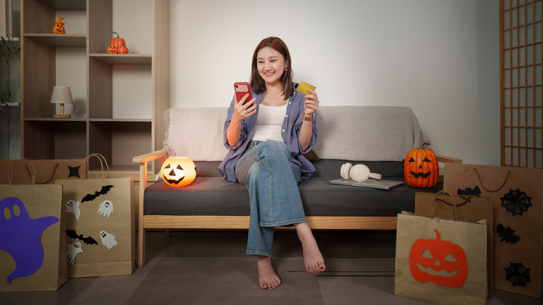 A woman smiles while buying Halloween decor on her phone