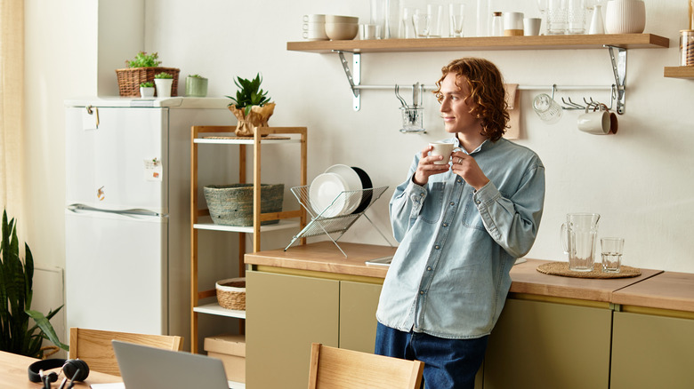 A person holds a mug while leaning against a countertop
