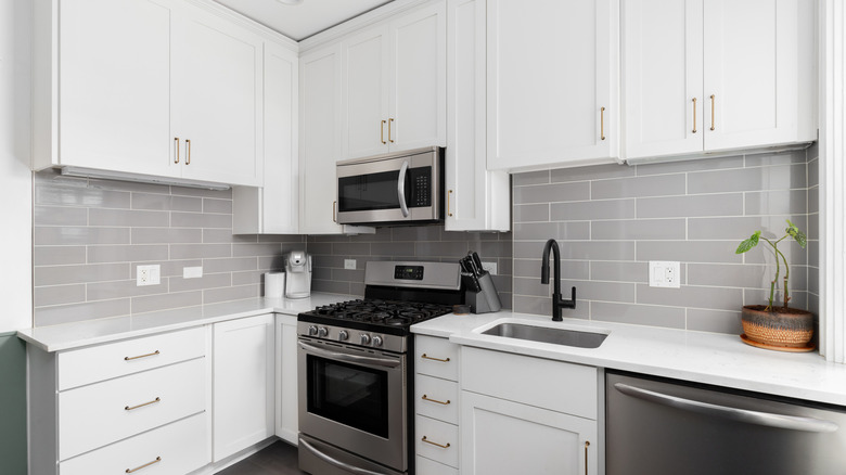 A white kitchen with white cabinets, countertops and a light gray backsplash